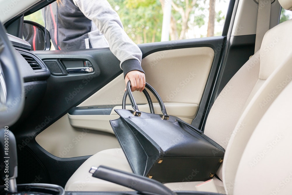 A person in a hoodie reaches into a car to pick up a handbag | Weygandt Law LLC